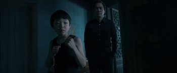 Movie still from “Shang-Chi and the Legend of the Ten Rings” (2021), directed by Destin Daniel Cretton – A man standing next to a woman in a dark room; Medium shot, Over the shoulder angle