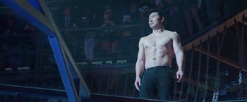 Movie still from “Shang-Chi and the Legend of the Ten Rings” (2021), directed by Destin Daniel Cretton – A man standing in front of an audience with his shirt off; Medium shot, Low angle