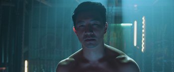Movie still from “Shang-Chi and the Legend of the Ten Rings” (2021), directed by Destin Daniel Cretton – A shirtless man in a dark room looking at the camera; Close Up shot, Low angle