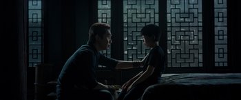 Movie still from “Shang-Chi and the Legend of the Ten Rings” (2021), directed by Destin Daniel Cretton – A man sitting next to a young boy in front of a window; Medium shot, Over the shoulder angle
