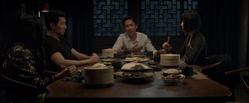 Movie still from “Shang-Chi and the Legend of the Ten Rings” (2021), directed by Destin Daniel Cretton – A group of people sitting at a table eating food; Medium shot, Over the shoulder angle