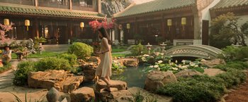 Movie still from “Shang-Chi and the Legend of the Ten Rings” (2021), directed by Destin Daniel Cretton – A woman in a dress walking across a pond in a garden; Extreme Wide shot, High angle