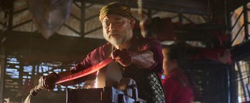 Movie still from “Shang-Chi and the Legend of the Ten Rings” (2021), directed by Destin Daniel Cretton – An older man wearing a head scarf is working with a piece of metal; Medium shot, Low angle