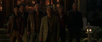 Movie still from “Shang-Chi and the Legend of the Ten Rings” (2021), directed by Destin Daniel Cretton – A group of men standing next to each other in front of a building; Medium shot, Over the shoulder angle