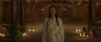 Movie still from “Shang-Chi and the Legend of the Ten Rings” (2021), directed by Destin Daniel Cretton – A woman in a white bathrobe standing in front of candles; Medium shot, Over the shoulder angle