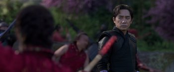Movie still from “Shang-Chi and the Legend of the Ten Rings” (2021), directed by Destin Daniel Cretton – A man holding a baseball bat while standing in front of a group of people; Close Up shot, Over the shoulder angle