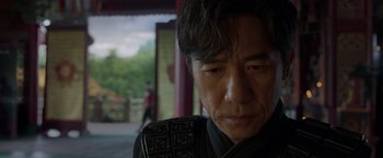 Movie still from “Shang-Chi and the Legend of the Ten Rings” (2021), directed by Destin Daniel Cretton – A person wearing a suit and tie; Close Up shot, Over the shoulder angle