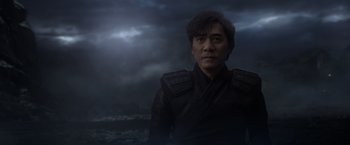Movie still from “Shang-Chi and the Legend of the Ten Rings” (2021), directed by Destin Daniel Cretton – A man in a black jacket standing in front of a body of water; Medium shot, Over the shoulder angle