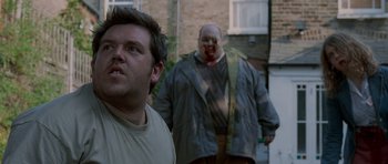Movie still from “Shaun of the Dead” (2004), directed by Edgar Wright – A man standing next to another man in a yard; Medium shot, Over the shoulder angle