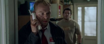 Movie still from “Shaun of the Dead” (2004), directed by Edgar Wright – A man holding a phone up to his ear while standing next to another man; Close Up shot, Over the shoulder angle