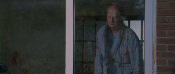 Movie still from “Shaun of the Dead” (2004), directed by Edgar Wright – A man in a robe standing in front of a window with blood on it; Medium shot, Over the shoulder angle