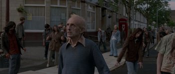 Movie still from “Shaun of the Dead” (2004), directed by Edgar Wright – An older man walking down a street with a crowd of people; Wide shot, Over the shoulder angle