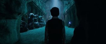 Movie still from “Shazam!” (2019), directed by David F. Sandberg – A man standing in a dark room with a light shining on him; Wide shot, Over the shoulder angle