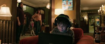 Movie still from “Shazam!” (2019), directed by David F. Sandberg – A young boy with headphones on looking at a laptop computer; Medium shot, Over the shoulder angle