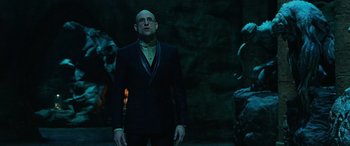 Movie still from “Shazam!” (2019), directed by David F. Sandberg – A bald man in a black suit standing in front of a stone wall; Medium shot, Low angle