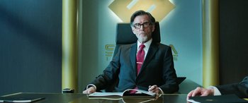 Movie still from “Shazam!” (2019), directed by David F. Sandberg – A man sitting at a desk in front of an open book; Medium shot, Over the shoulder angle