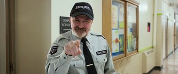 Movie still from “Shazam!” (2019), directed by David F. Sandberg – A man in a security uniform pointing to his shirt; Medium shot, Over the shoulder angle