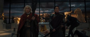 Movie still from “Shazam! Fury of the Gods” (2023), directed by David F. Sandberg – Two women dressed in costumes stand next to each other in front of a window; Medium shot, Over the shoulder angle