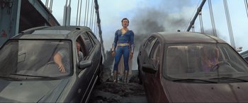 Movie still from “Shazam! Fury of the Gods” (2023), directed by David F. Sandberg – A man dressed as superman standing in front of two cars; Wide shot, Low angle