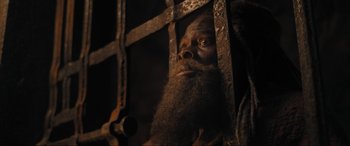 Movie still from “Shazam! Fury of the Gods” (2023), directed by David F. Sandberg – A man with a long beard is looking through bars; Close Up shot, High angle