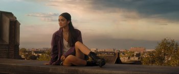 Movie still from “Shazam! Fury of the Gods” (2023), directed by David F. Sandberg – A woman sitting on a ledge in front of a city skyline; Medium shot, Low angle
