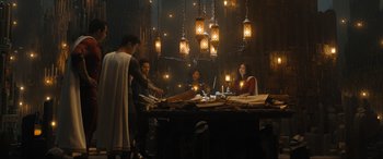 Movie still from “Shazam! Fury of the Gods” (2023), directed by David F. Sandberg – A group of people sitting at a table in a dark room; Wide shot, High angle