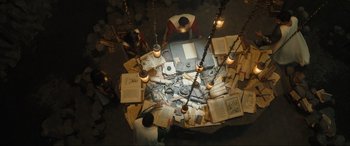Movie still from “Shazam! Fury of the Gods” (2023), directed by David F. Sandberg – An overhead view of a group of people sitting at a table with books; Wide shot, High angle