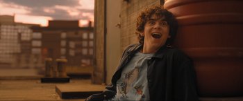 Movie still from “Shazam! Fury of the Gods” (2023), directed by David F. Sandberg – A young man with a goofy shirt is smiling; Medium shot, Low angle