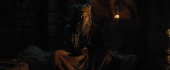 Movie still from “Shazam! Fury of the Gods” (2023), directed by David F. Sandberg – A man with a long beard sitting in a cave at night; Medium shot, High angle