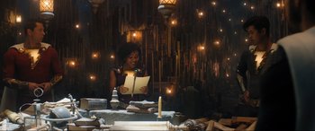 Movie still from “Shazam! Fury of the Gods” (2023), directed by David F. Sandberg – A woman standing in front of a candle and a book; Medium shot, Over the shoulder angle