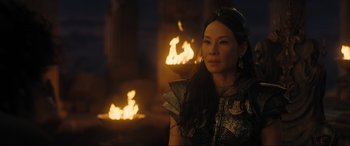 Movie still from “Shazam! Fury of the Gods” (2023), directed by David F. Sandberg – A woman in a costume standing in front of a fire pit; Close Up shot, Over the shoulder angle