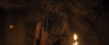 Movie still from “Shazam! Fury of the Gods” (2023), directed by David F. Sandberg – A man with dreadlocks is standing in front of a fire; Medium shot, Low angle