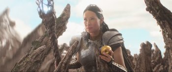 Movie still from “Shazam! Fury of the Gods” (2023), directed by David F. Sandberg – A woman holding an apple while wearing armor; Medium shot, Low angle