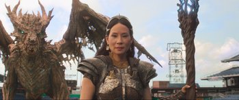 Movie still from “Shazam! Fury of the Gods” (2023), directed by David F. Sandberg – A woman dressed in a costume with a bird on top of her head; Medium shot, Low angle