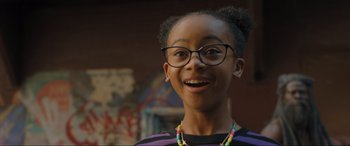 Movie still from “Shazam! Fury of the Gods” (2023), directed by David F. Sandberg – A young girl wearing glasses and smiling for the camera; Close Up shot, Over the shoulder angle