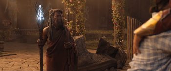 Movie still from “Shazam! Fury of the Gods” (2023), directed by David F. Sandberg – An old man with dreadlocks standing next to a couch; Medium shot, Over the shoulder angle