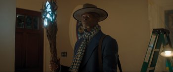 Movie still from “Shazam! Fury of the Gods” (2023), directed by David F. Sandberg – A man in a suit and hat holding a wooden staff; Medium shot, Low angle