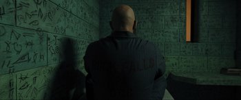 Movie still from “Shazam! Fury of the Gods” (2023), directed by David F. Sandberg – A bald man in a dark room with graffiti written on the wall; Medium shot, Over the shoulder angle