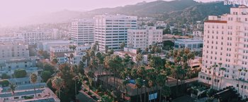 Movie still from “Shelter in Place” (2021), directed by Connor Martin – An aerial view of palm trees and buildings in a city; Extreme Wide shot, Low angle