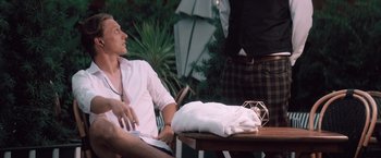 Movie still from “Shelter in Place” (2021), directed by Connor Martin – A man sitting at a table with a towel on top of it; Medium shot, Over the shoulder angle