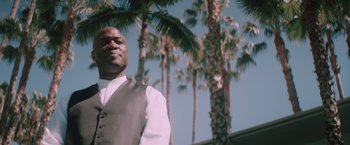 Movie still from “Shelter in Place” (2021), directed by Connor Martin – A man standing in front of some palm trees; Medium shot, Low angle