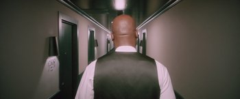 Movie still from “Shelter in Place” (2021), directed by Connor Martin – A man in a white shirt and black vest walking down a hallway; Medium shot, Low angle