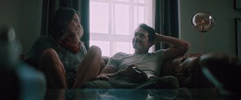 Movie still from “Shelter in Place” (2021), directed by Connor Martin – A man and a woman sitting on a couch in front of a window; Medium shot, Low angle