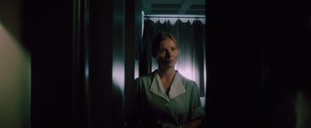 Movie still from “Shelter in Place” (2021), directed by Connor Martin – A woman standing in front of a window in a room; Medium shot, Low angle