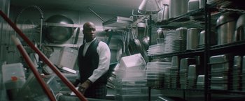 Movie still from “Shelter in Place” (2021), directed by Connor Martin – A man standing in front of stacks of plastic containers; Medium shot, Low angle