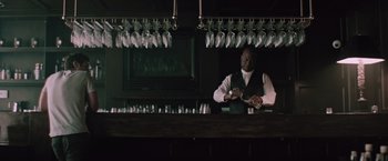 Movie still from “Shelter in Place” (2021), directed by Connor Martin – A man sitting at a bar looking at his watch; Medium shot, Low angle