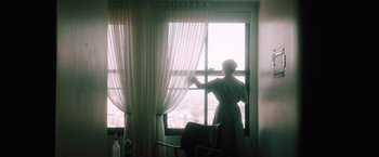 Movie still from “Shelter in Place” (2021), directed by Connor Martin – A person standing in front of a window looking outside; Wide shot, Low angle