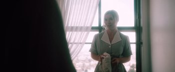 Movie still from “Shelter in Place” (2021), directed by Connor Martin – A woman standing in front of a window holding a towel; Medium shot, Over the shoulder angle