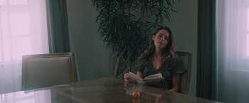 Movie still from “Shelter in Place” (2021), directed by Connor Martin – A woman sitting at a table with an open book; Medium shot, Over the shoulder angle