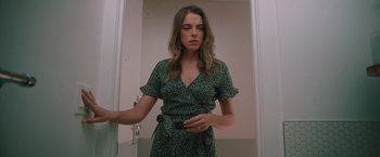 Movie still from “Shelter in Place” (2021), directed by Connor Martin – A woman in a green and black dress standing in front of a mirror; Medium shot, Low angle